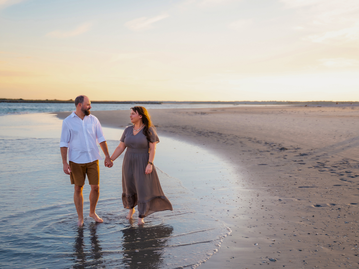 Couple walking hand in hand along the shoreline at sunset on a calm beach.