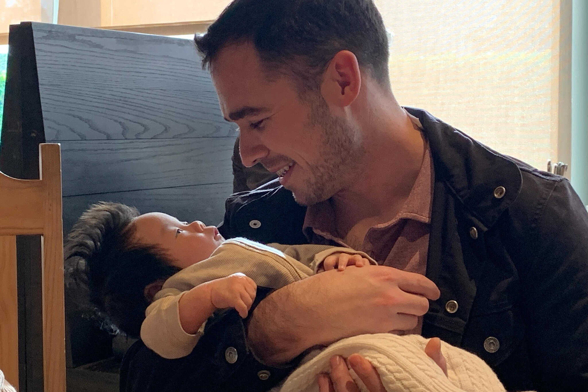 Man cradling a baby, smiling while looking at the infant in his arms indoors