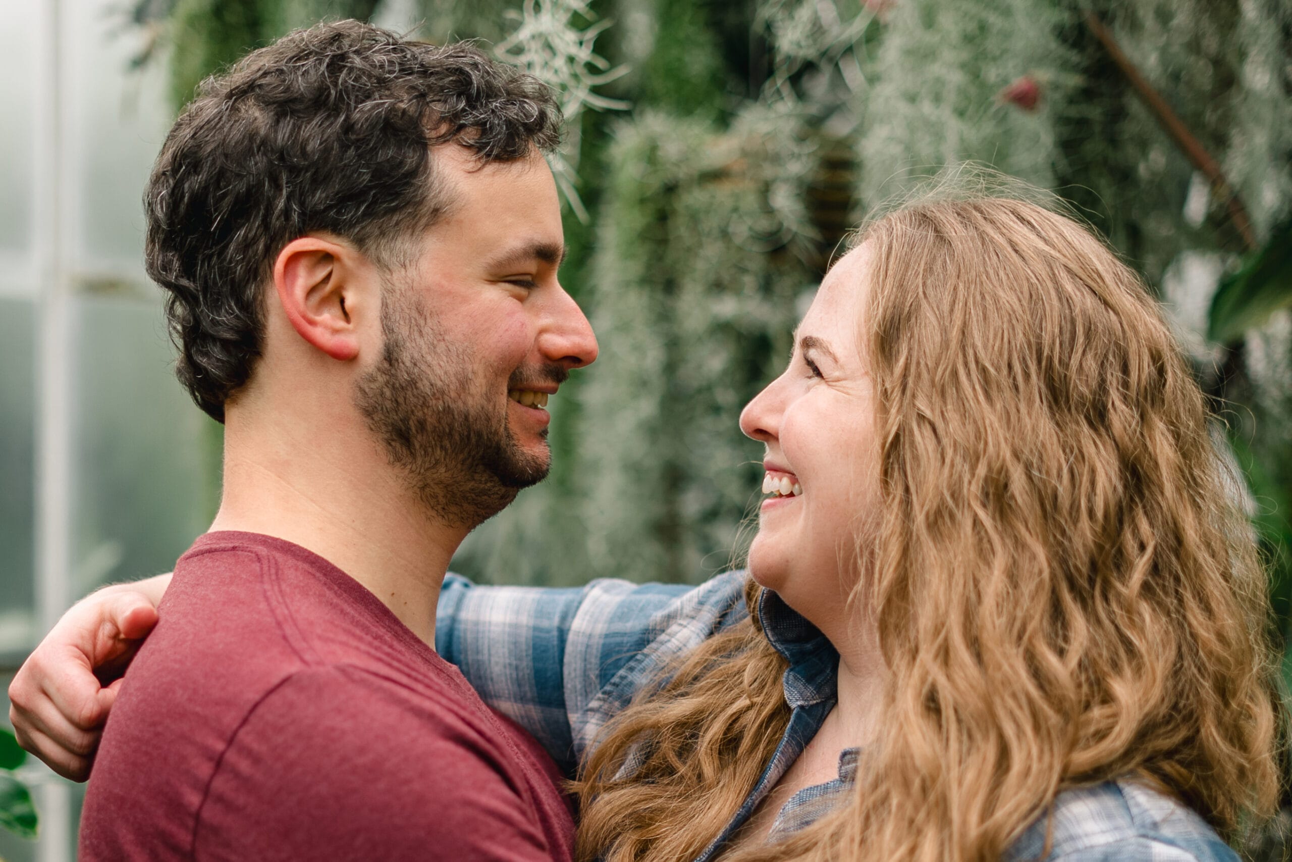 Close-up of a smiling couple embracing, faces close together with greenery in the background.
