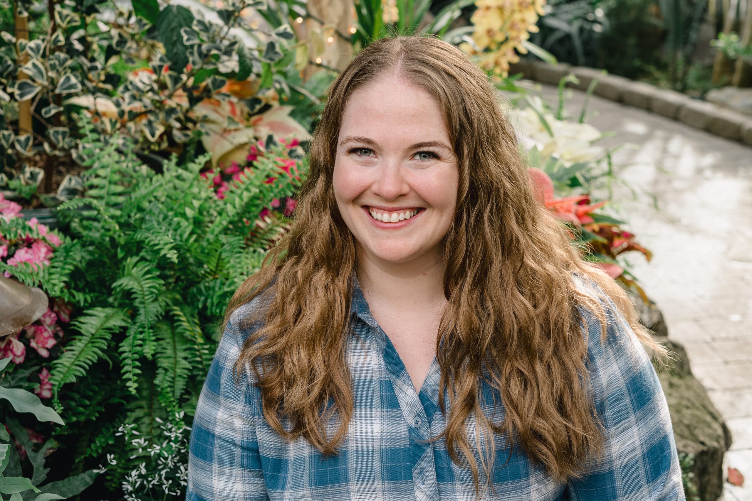Smiling young woman with long wavy hair outdoors in a lush garden.
