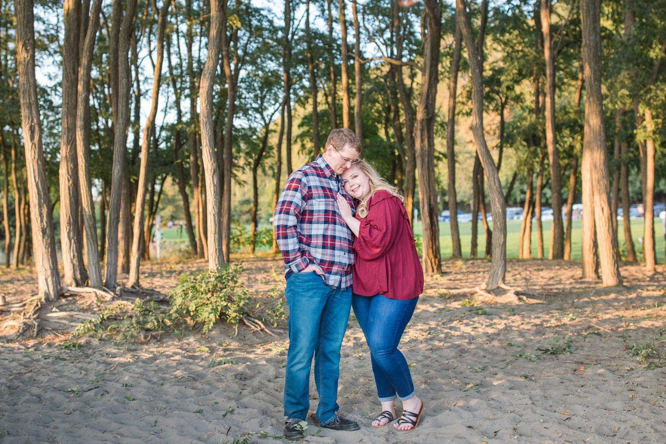 Couple embracing in a wooded park, smiling at the camera.