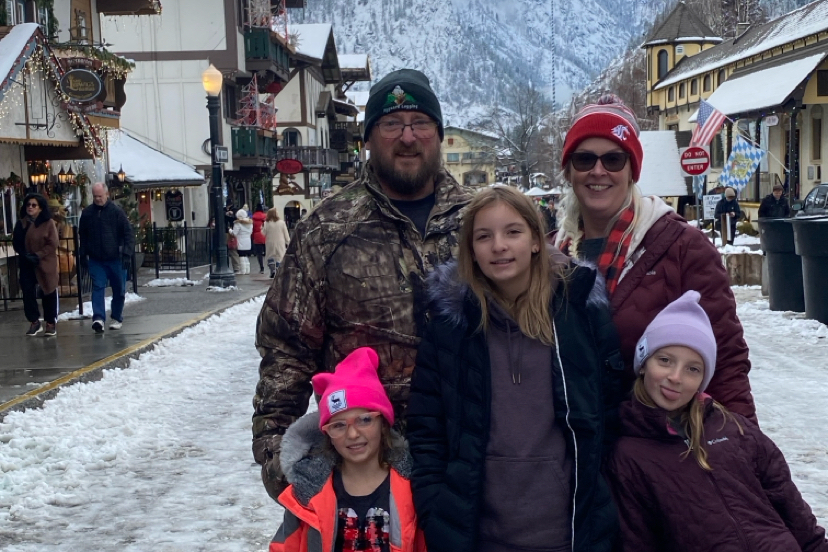 Family of five posing for a photo on a snowy village street with shops and mountains in the background.