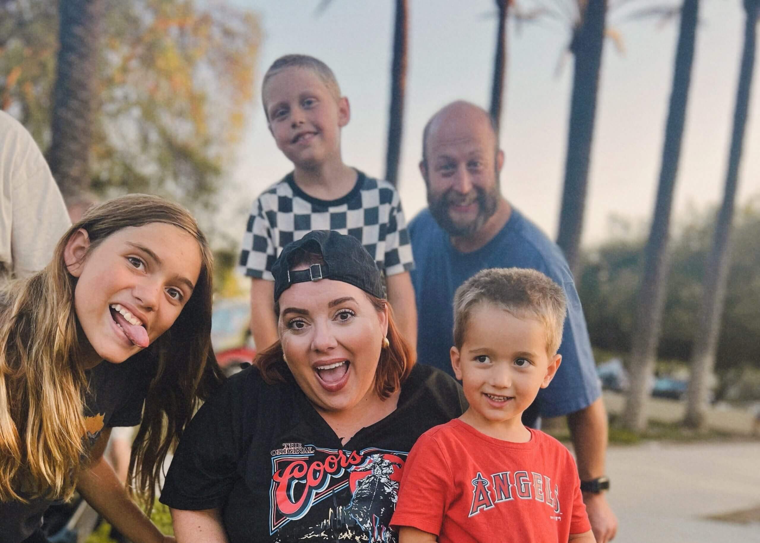 Group of smiling people posing for a selfie outdoors, with palm trees in the background.