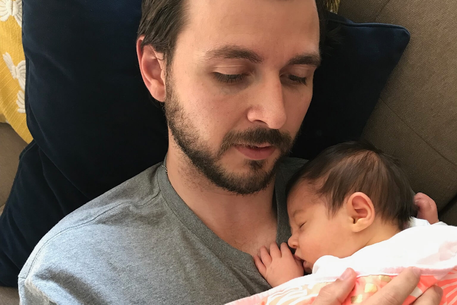 Father lying on a couch, cradling a sleeping newborn against his chest