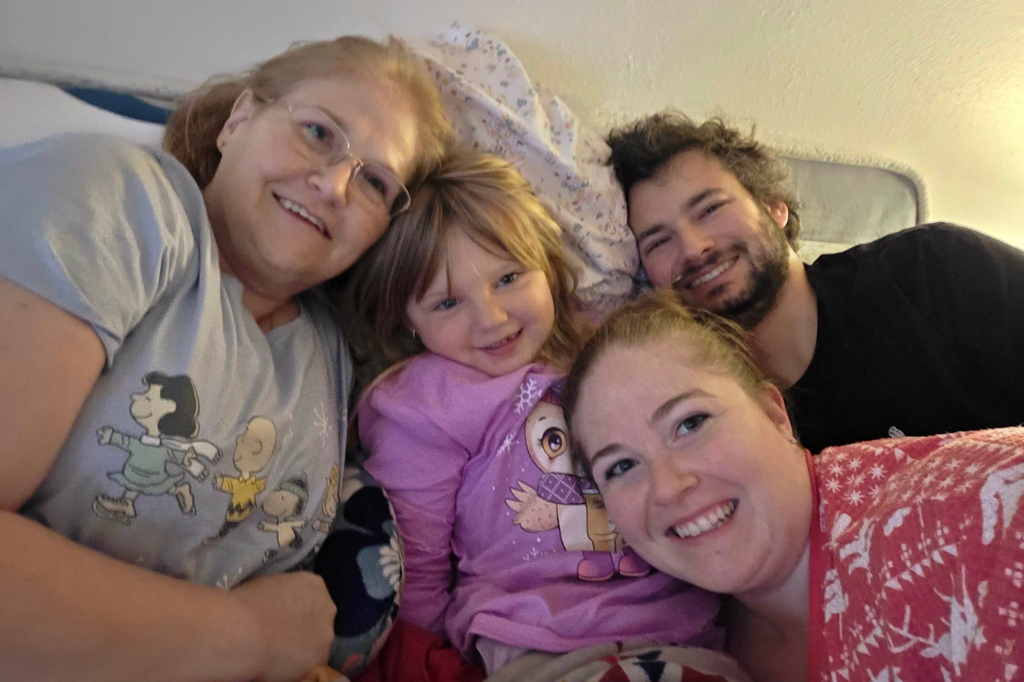Smiling family posing closely for a selfie on a sofa, with a woman wearing glasses, two children, and a man.