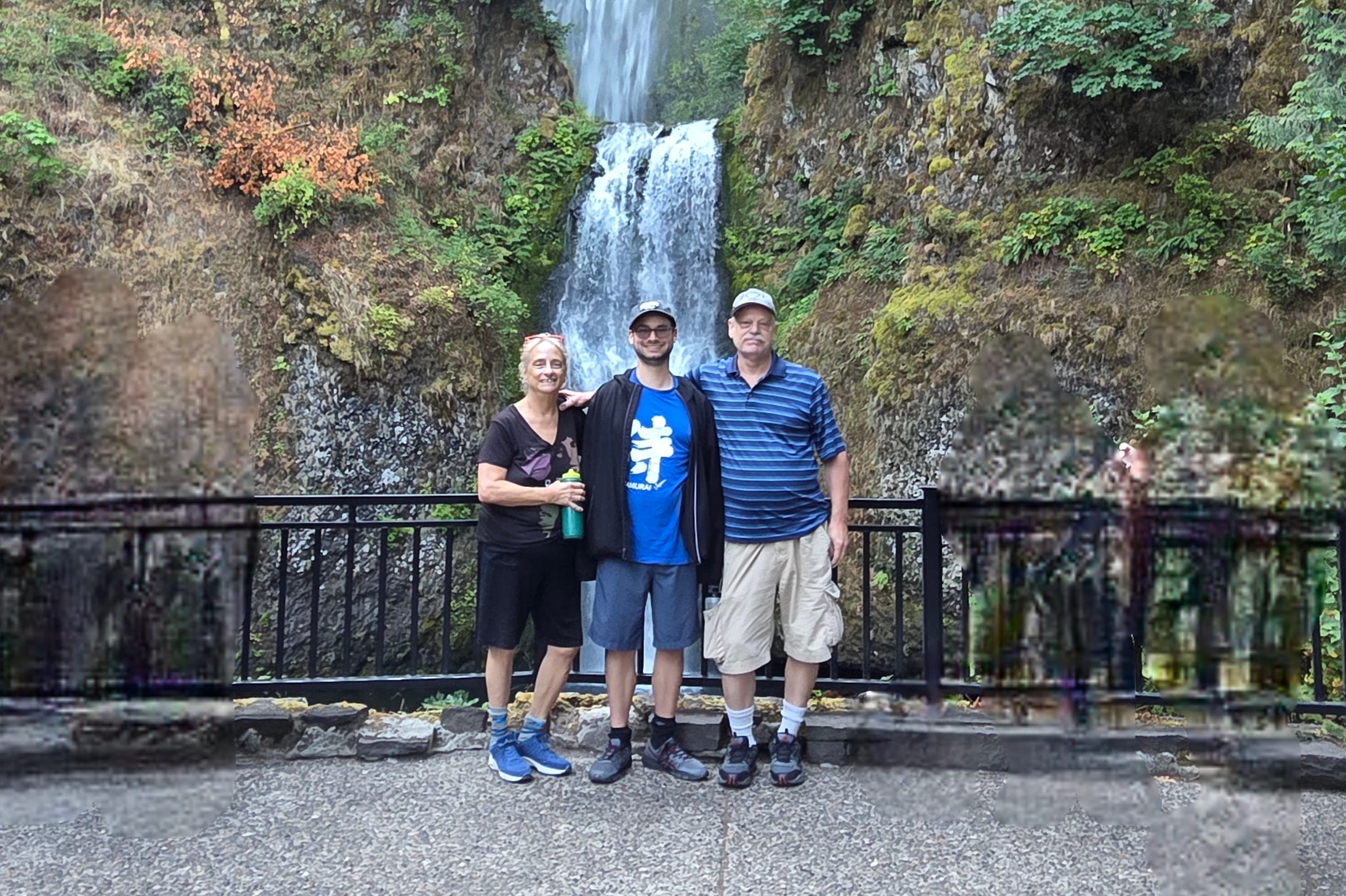 Three people posing together in front of a waterfall with a railing behind them.