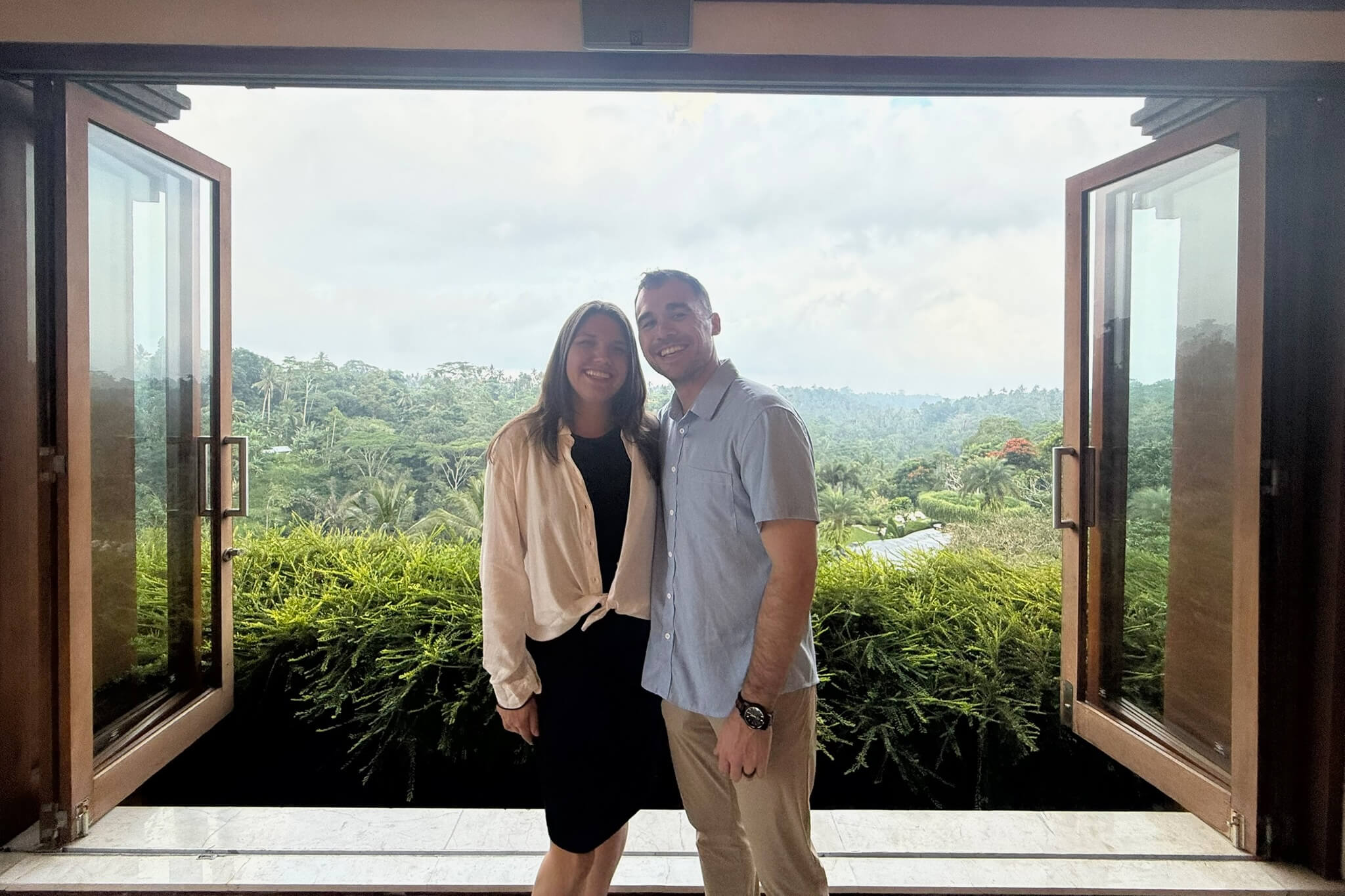 Smiling couple standing in an open doorway with a lush tropical garden outside.