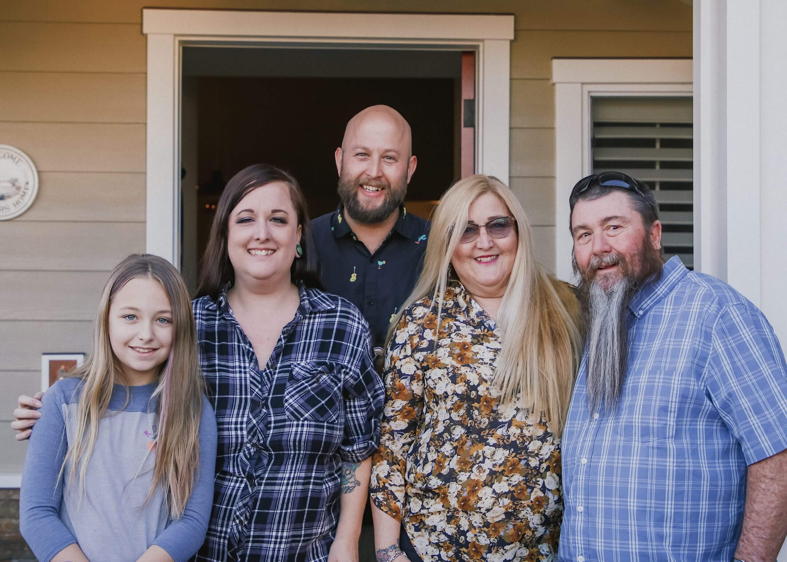 Five people stand closely together on a front porch, smiling at the camera.