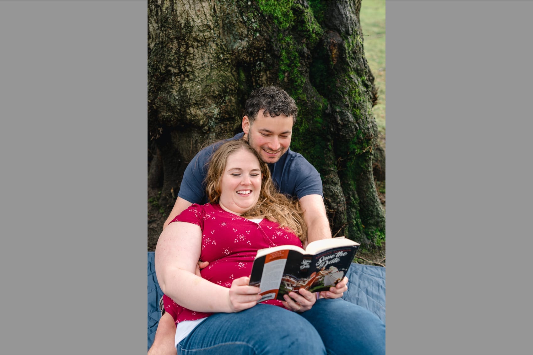 Smiling couple sitting outdoors under a mossy tree, reading a magazine together.