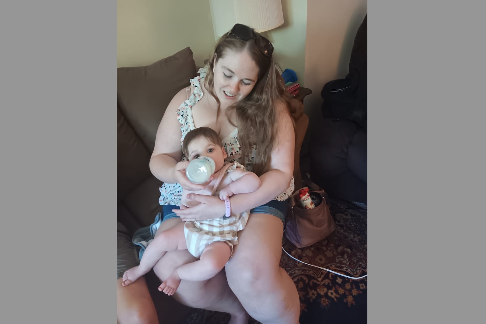 Woman on a couch bottle-feeds a baby, holding the infant close in her arms.