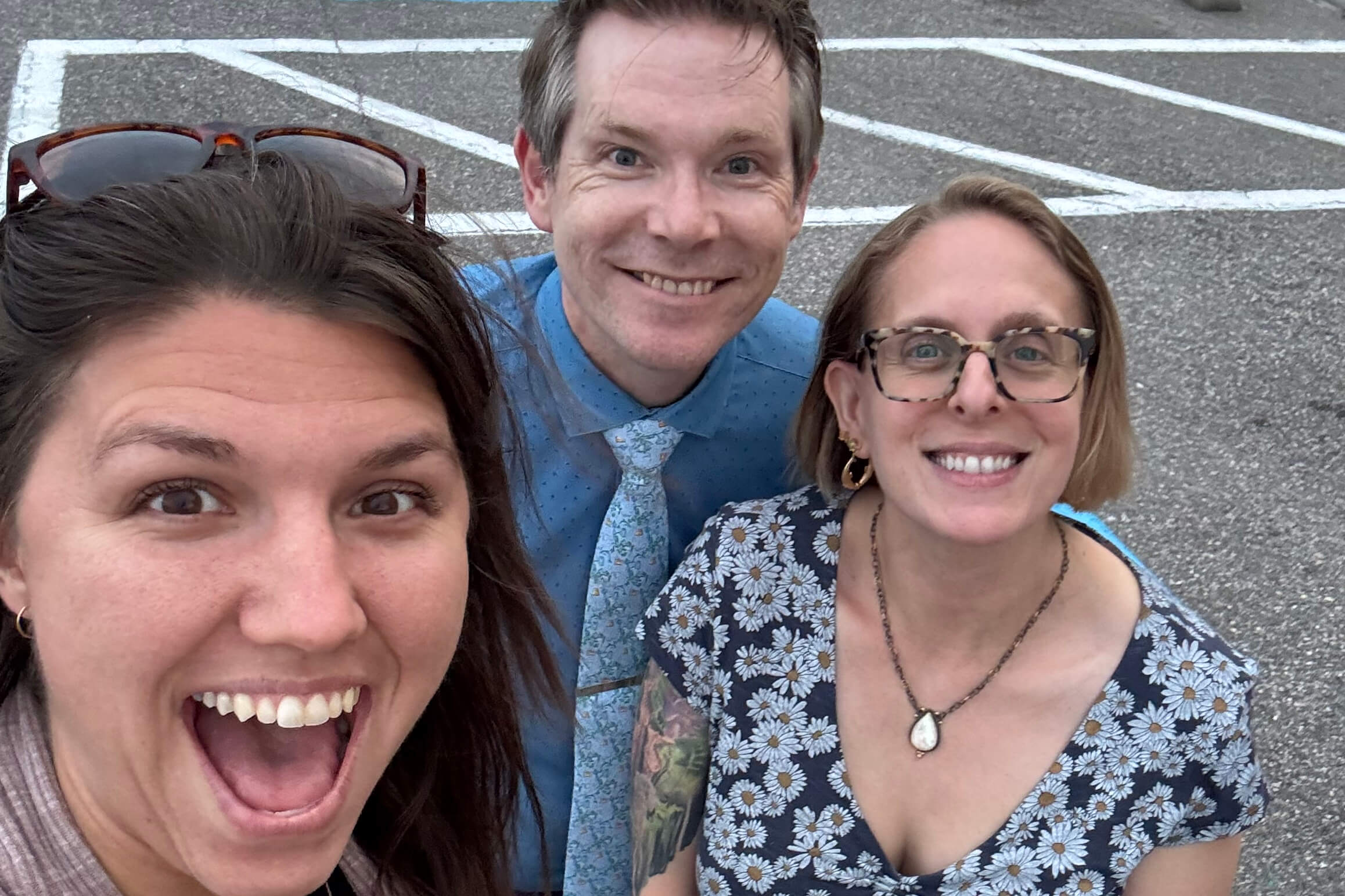 Three friends pose for a close-up selfie in a parking lot, all smiling at the camera.