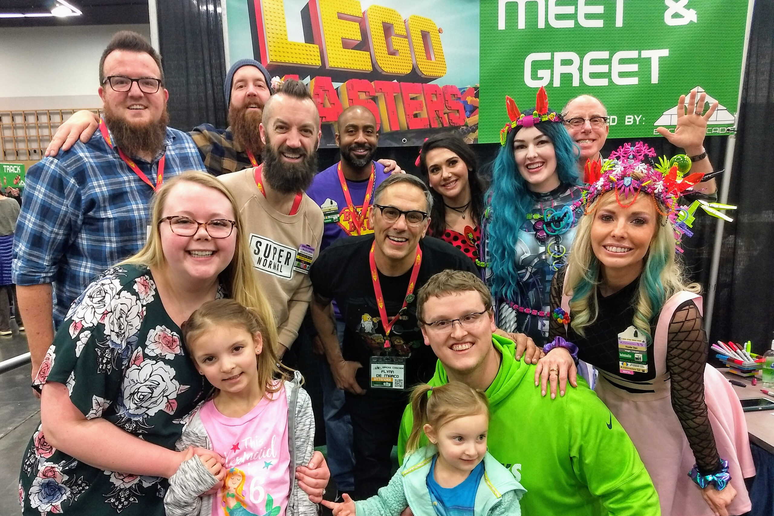 Group of adults and children posing together at a convention, some in colorful outfits and accessories, smiling at the camera.