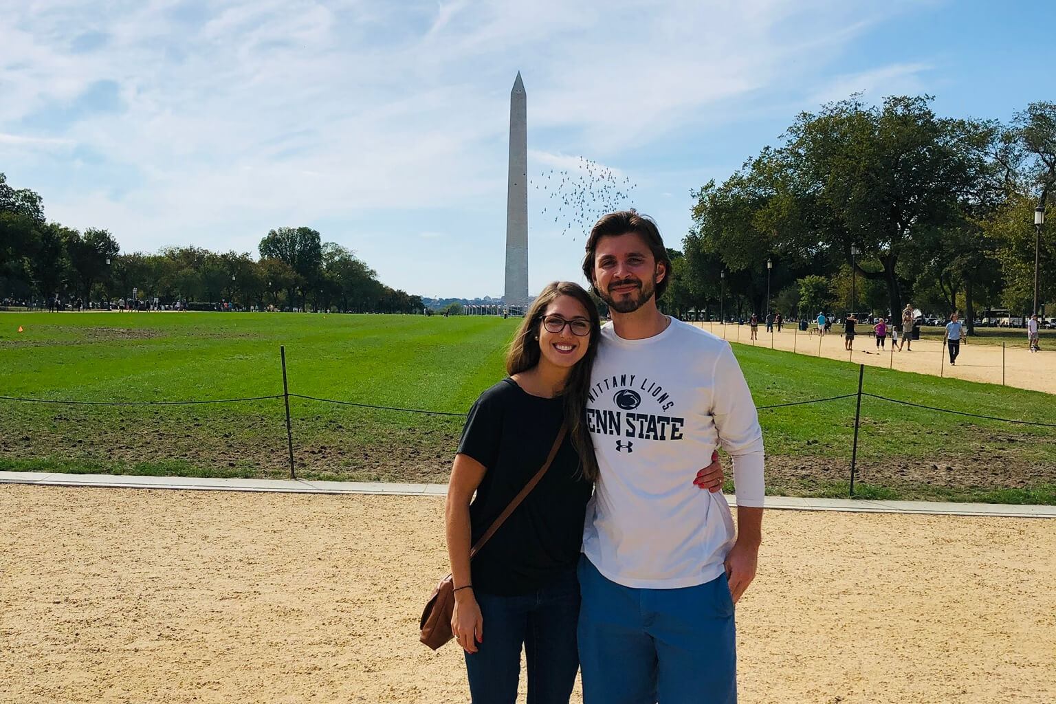 Smiling couple stands arm in arm on the National Mall with the Washington Monument in the background.