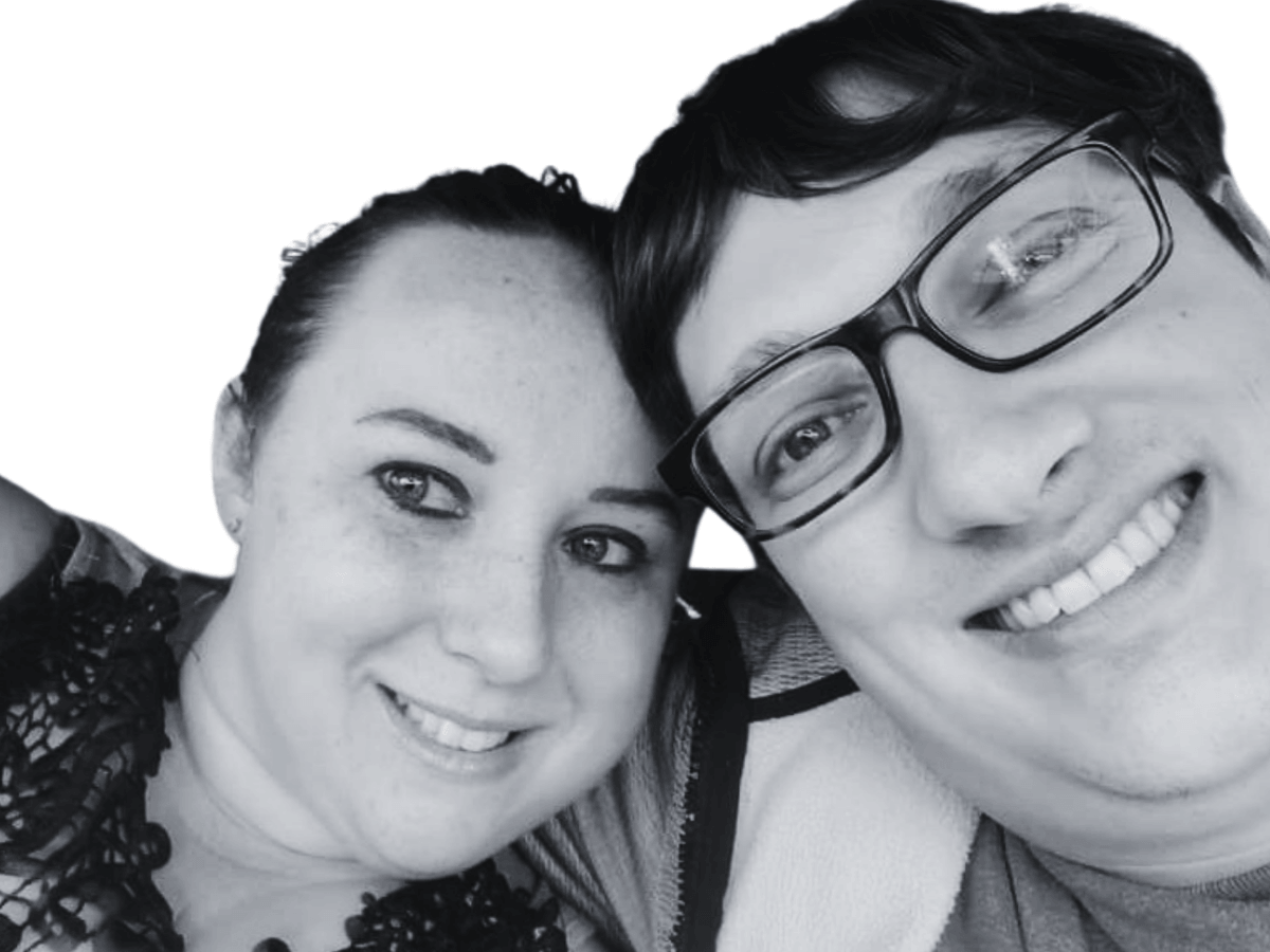 Smiling couple in a close-up selfie: woman on the left and man with glasses on the right, both looking at the camera (black-and-white).