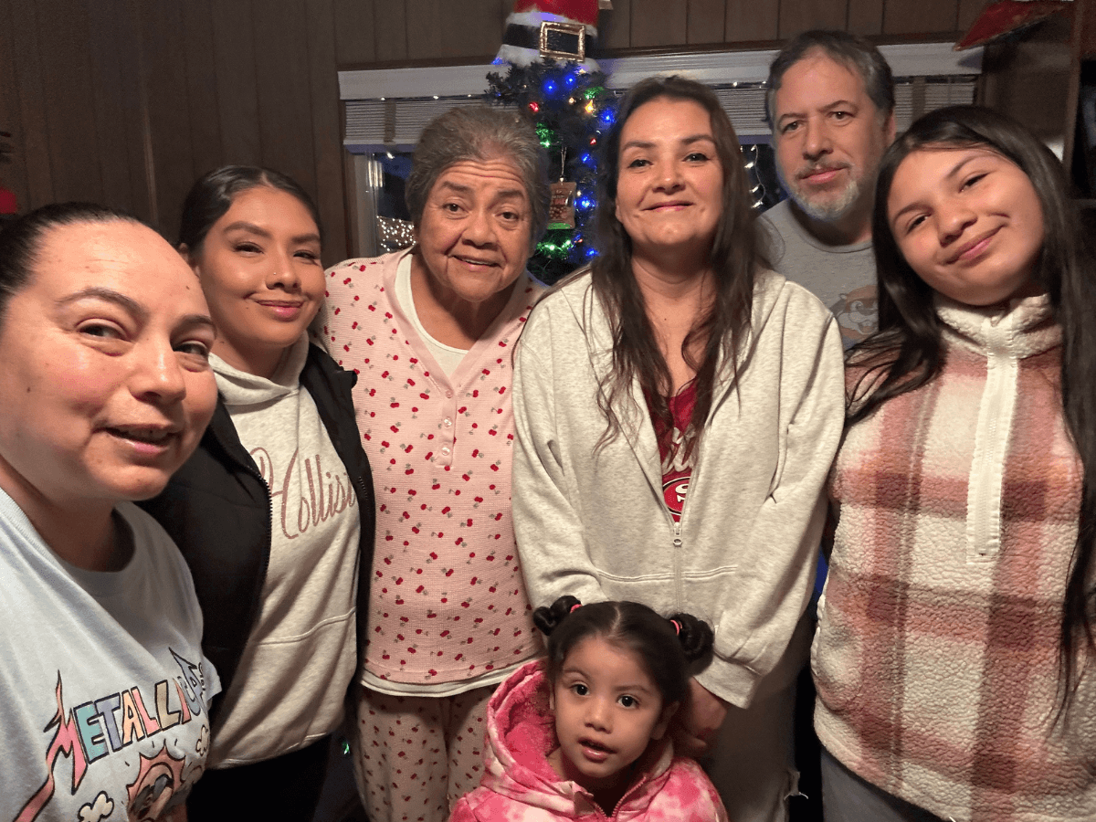 Seven family members pose for a holiday photo indoors, with a decorated Christmas tree in the background.