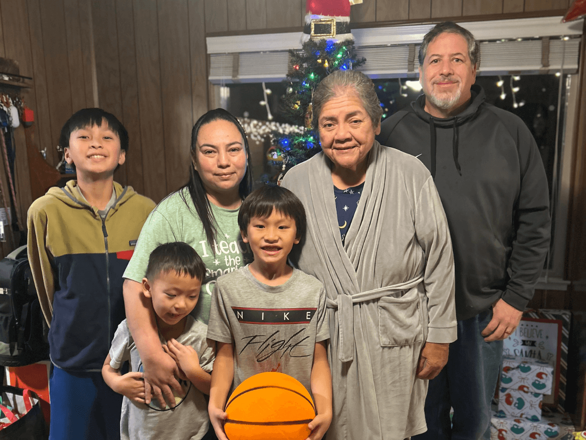 Family group in a living room posing by a Christmas tree; grandmother in a robe with parents and kids, one child holds a basketball.