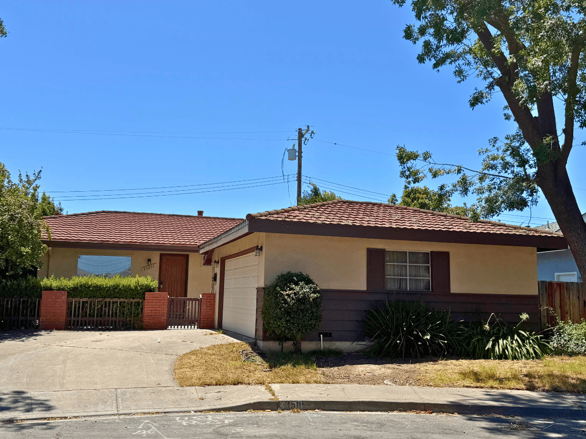 Front view of a single-story suburban house with a two-car garage, beige walls, dark brown trim, and a red tiled roof.