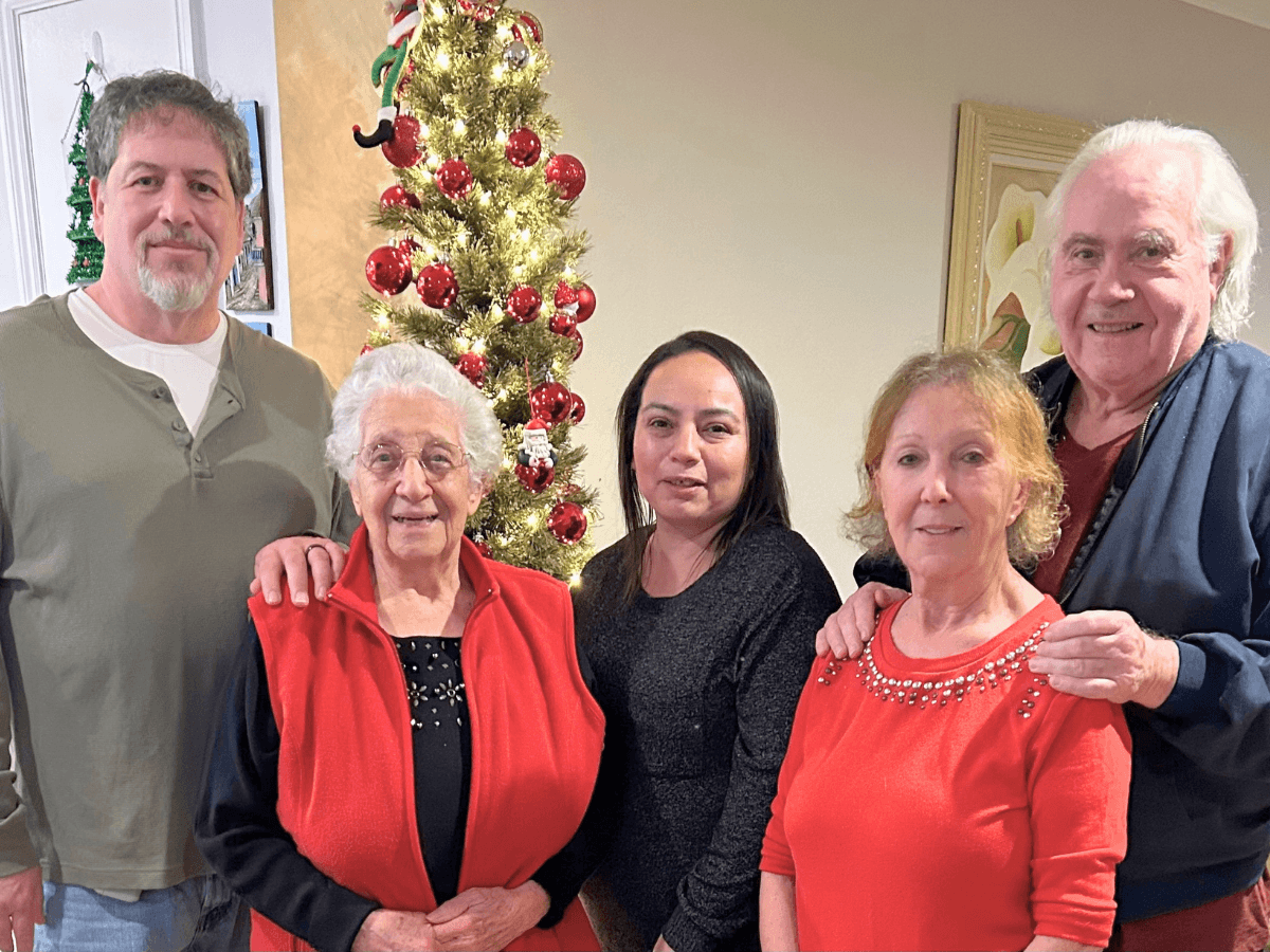 Five adults posing indoors in front of a lit Christmas tree with red ornaments.