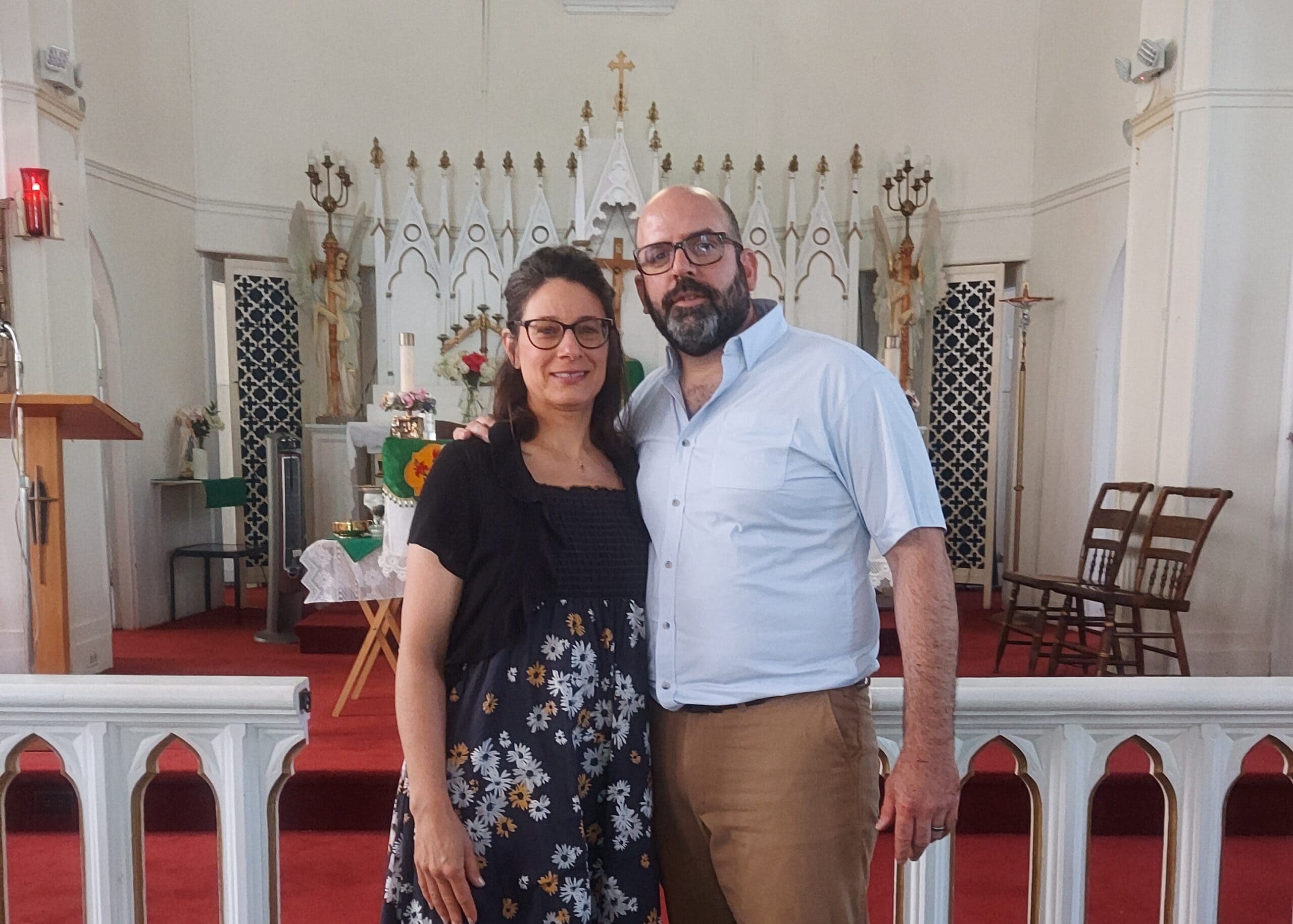 Couple posing together in a church, standing in front of an ornate white altar with candles and statues in the background.