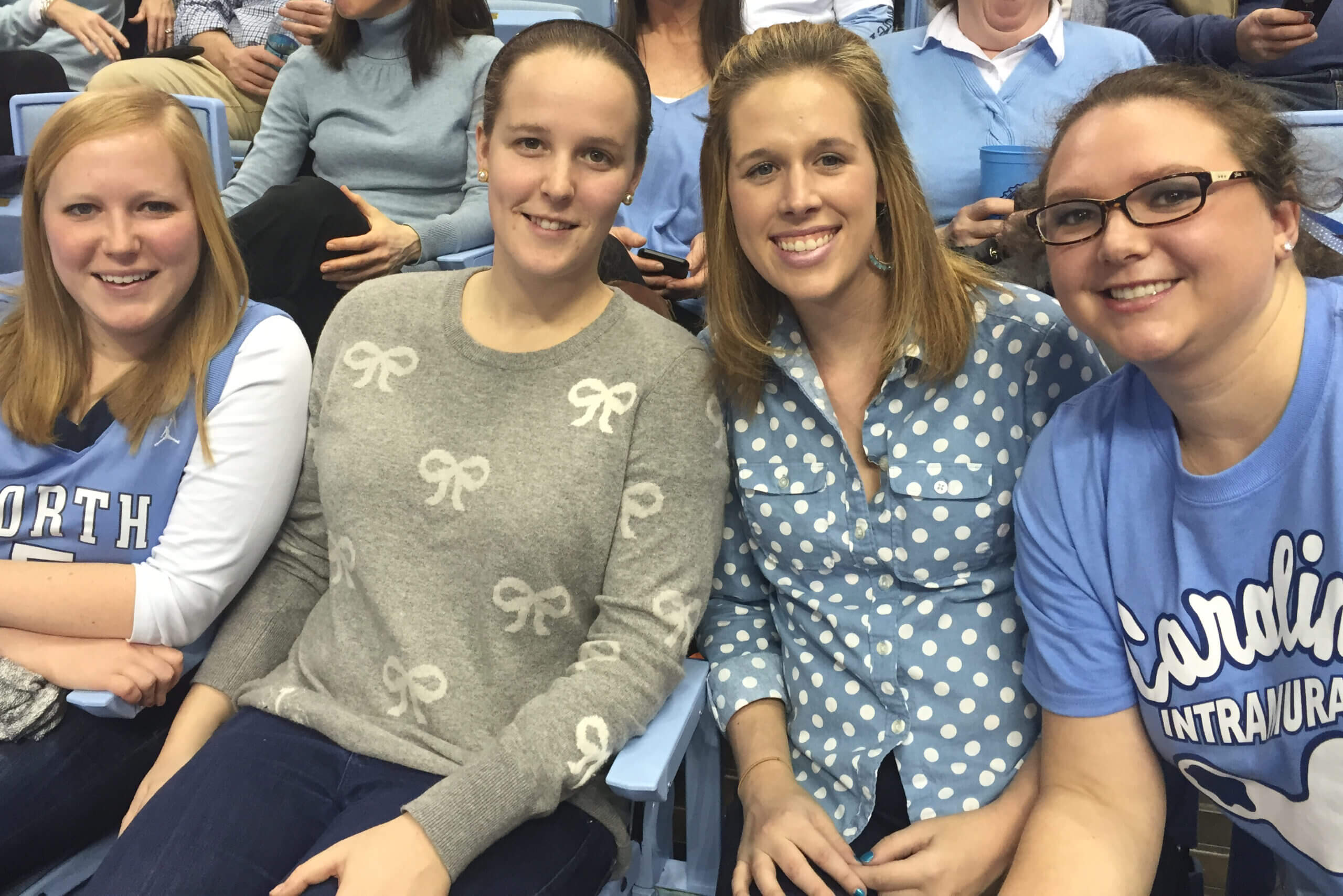 Four people seated in blue stadium seats, smiling for a group selfie at a sports event.