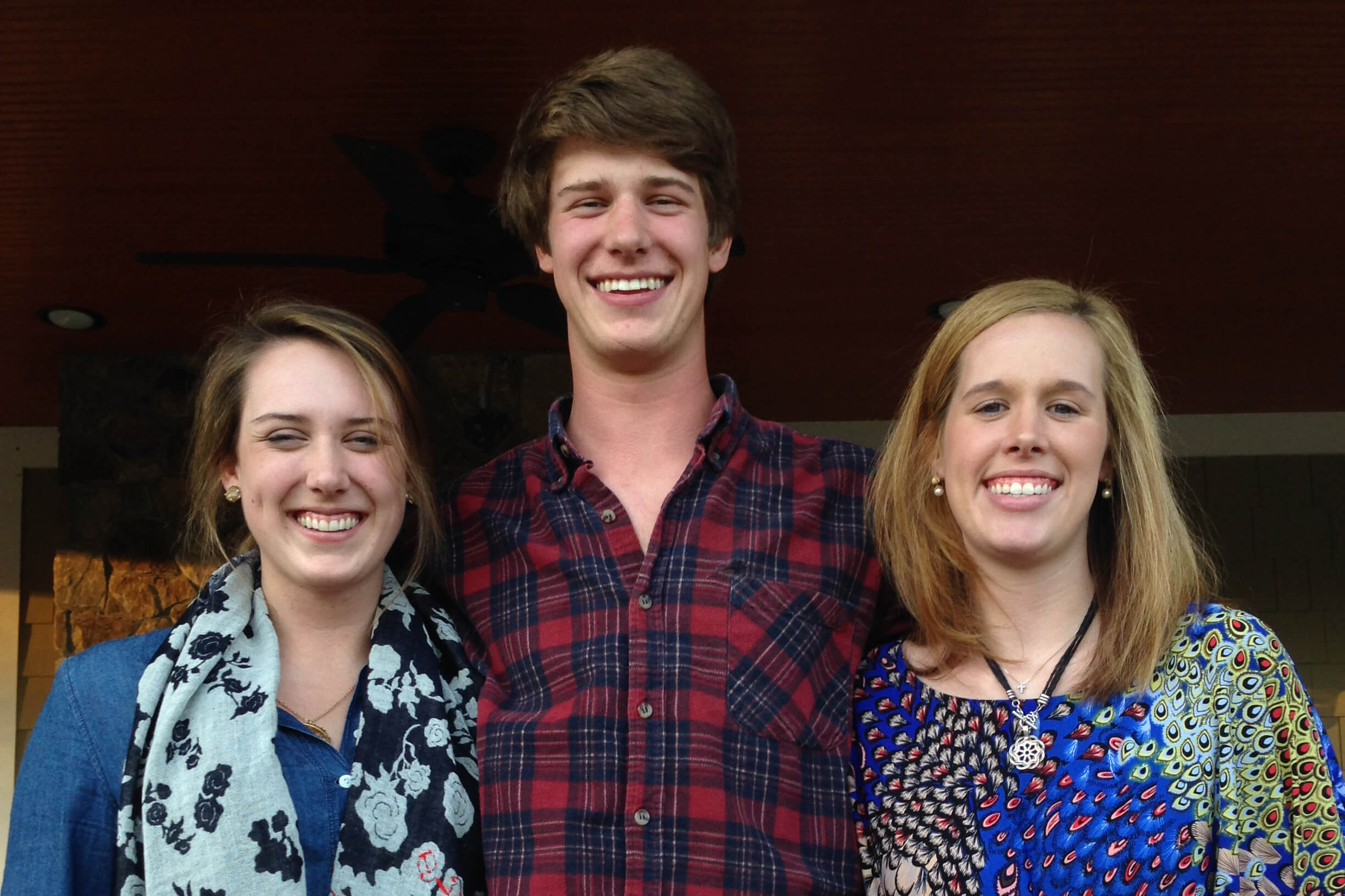 Three young adults smiling at the camera, standing side by side indoors.